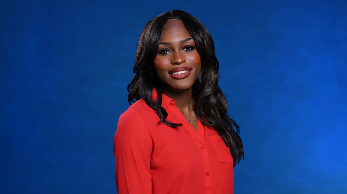 A confident woman with long wavy dark hair wearing a red blouse, smiling in front of a dark blue studio background.